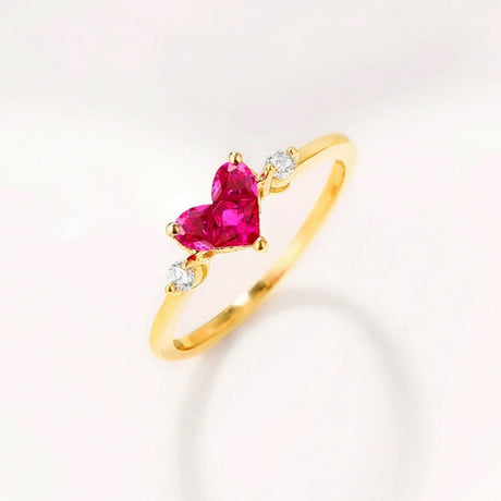 A 14K yellow gold ring with a heart-shaped natural ruby center stone and round diamond accents on a white background. | SARATTI
