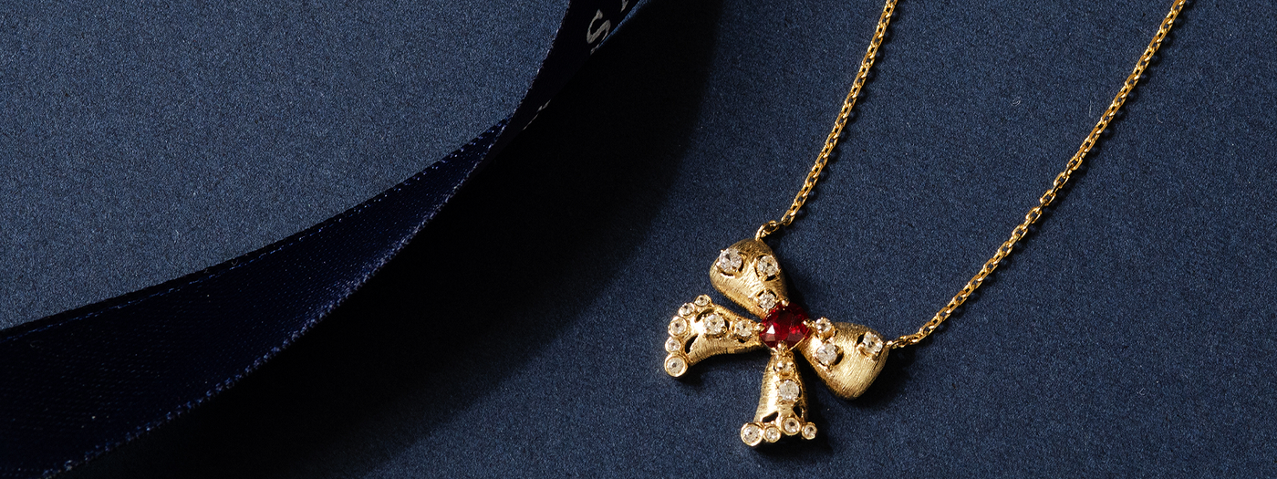 Gold necklace with a cross pendant featuring a red gemstone on a dark blue background | SARATTI Jewelry