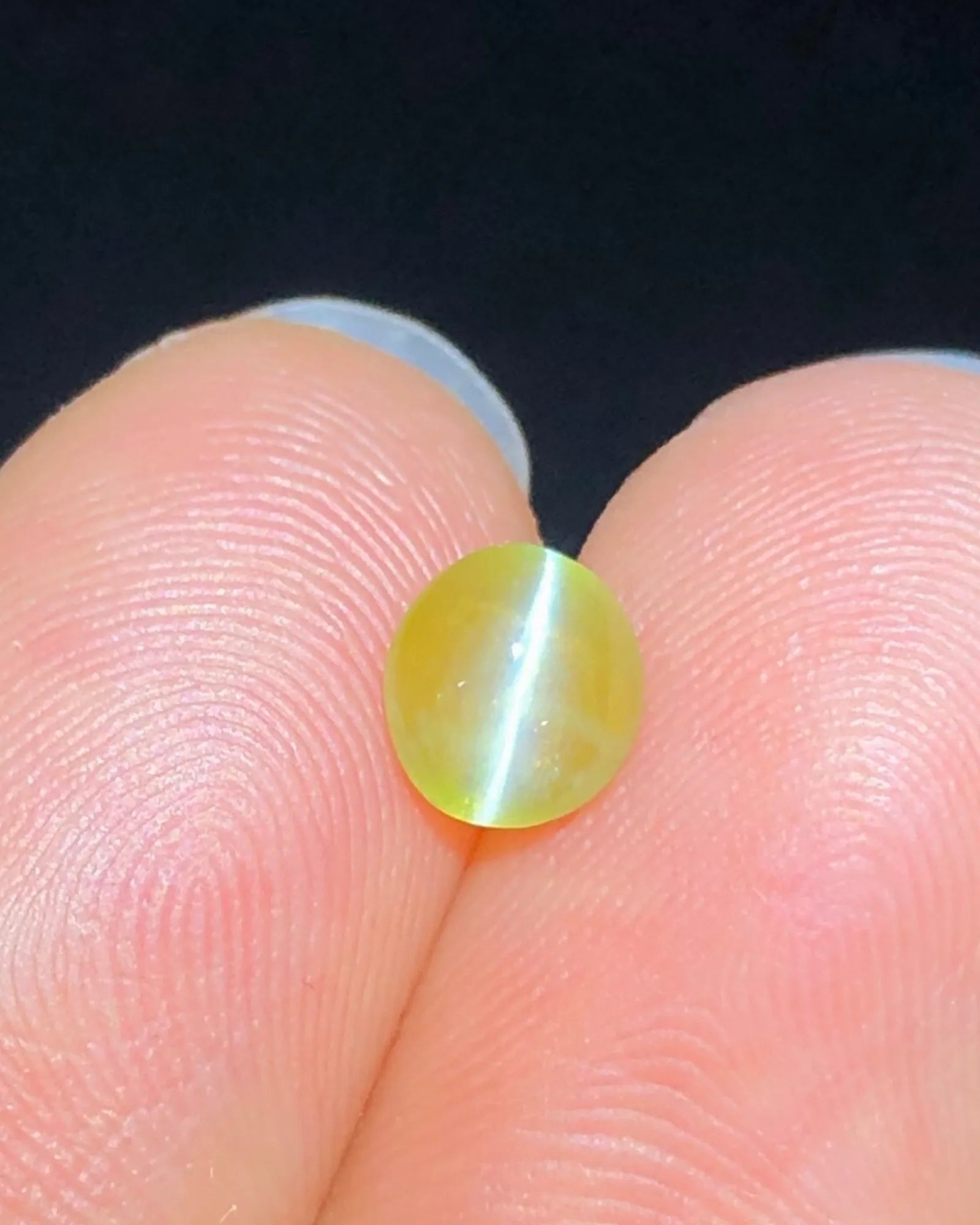 Close-up of 1.28 carat Yellowish Green Cat's-Eye Chrysoberyl showing a concentrated chatoyant band across the oval cabochon