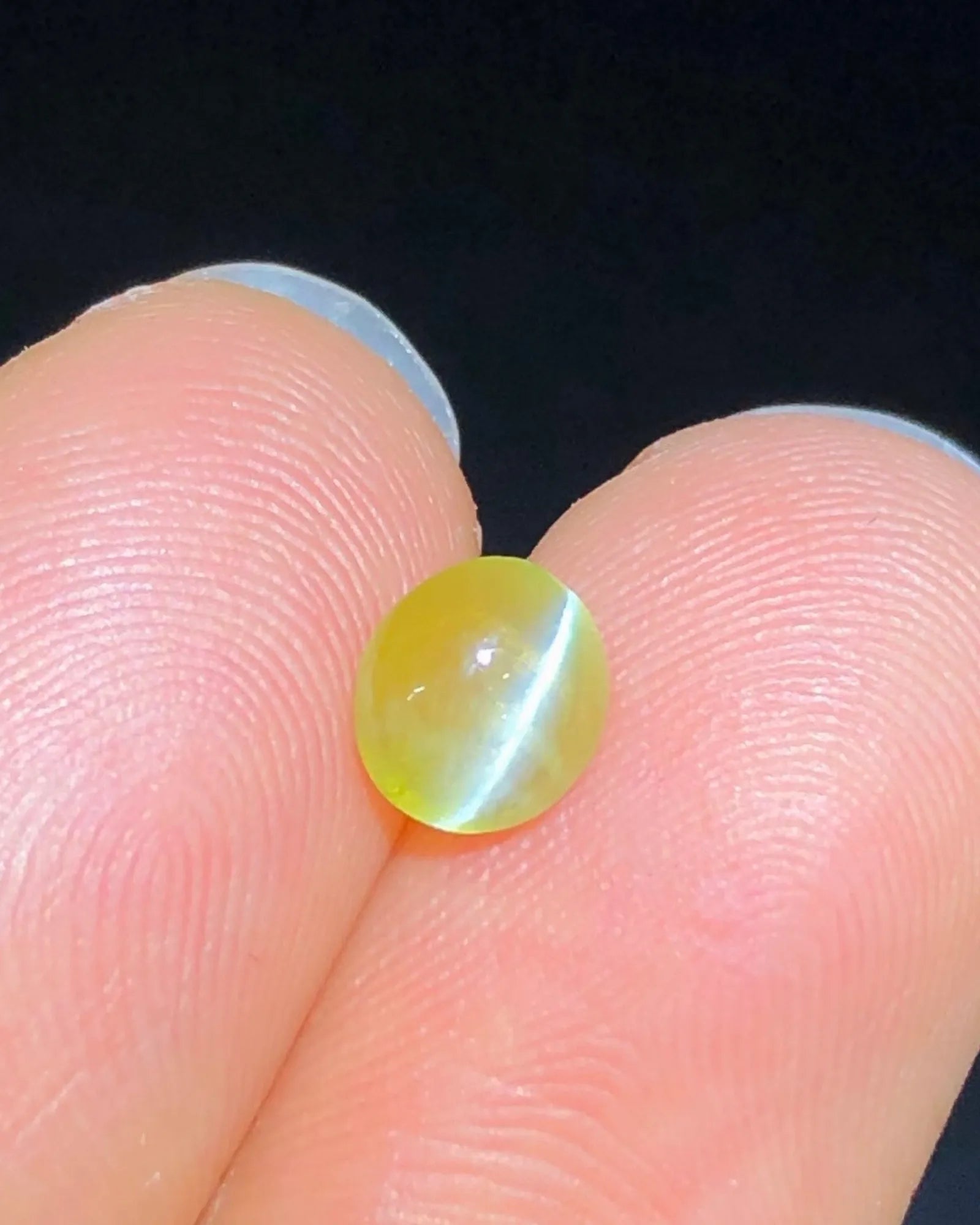 Close-up of 1.28 carat Yellowish Green Cat's-Eye Chrysoberyl showing a concentrated chatoyant band across the oval cabochon