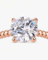 Colorless round moissanite ring framed by four rose gold prongs and rhythmic spherical detailing | SARATTI