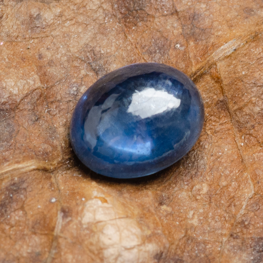Deep blue oval cabochon sapphire gemstone photographed on white background | SARATTI