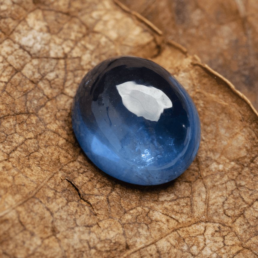 Genuine oval cabochon sapphire stone displayed on textured surface | SARATTI