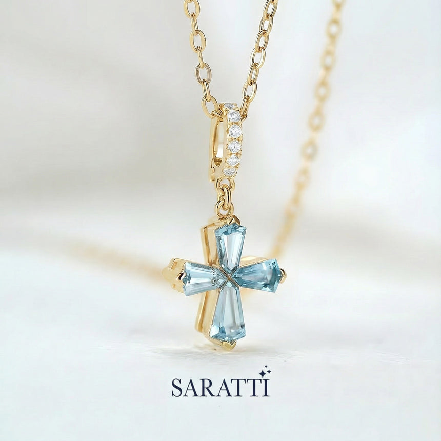 Gold necklace with a blue aquamarine gemstones designed into cross pendant on a light background, featuring the SARATTI brand.