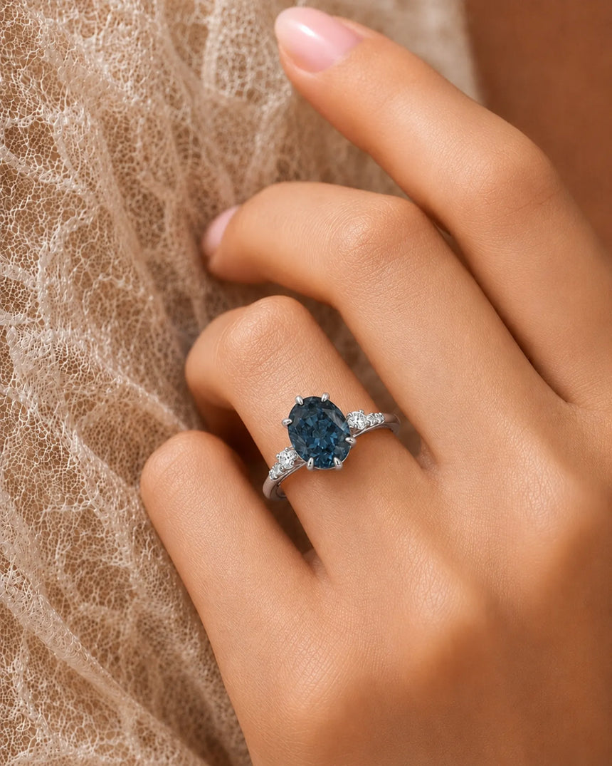 Oval blue moissanite center with colorless round side stones in 18K white gold | SARATTI