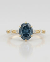 Oval blue moissanite center with colorless round side stones in 18K yellow gold | SARATTI