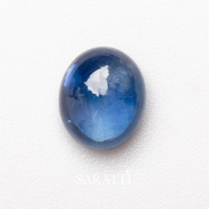Oval cabochon blue sapphire gemstone close-up on natural surface | SARATTI