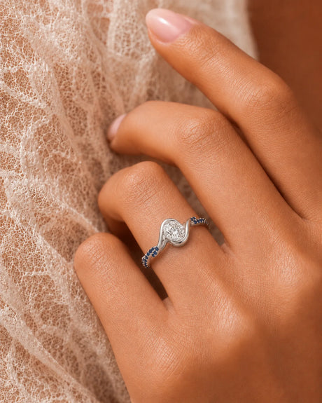 Oval moissanite bezel ring in platinum with twisted sapphire-set shoulders and open gallery | SARATTI