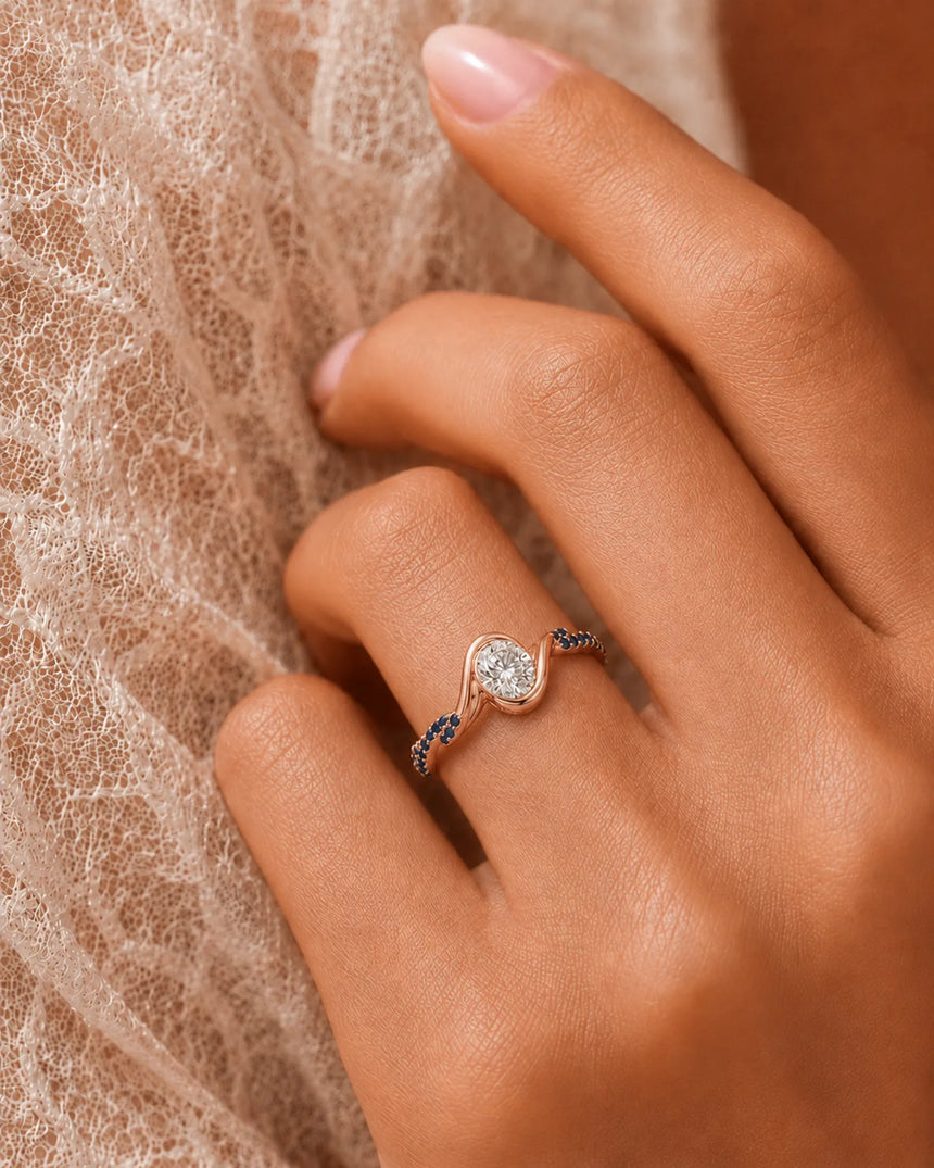 Oval moissanite bezel ring in rose gold with twisted sapphire-set shoulders and open gallery | SARATTI