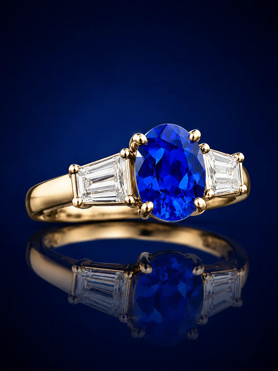 Elegant SARATTI sapphire and diamond three-stone ring shown at a 45-degree angle with polished gold setting and deep blue backdrop