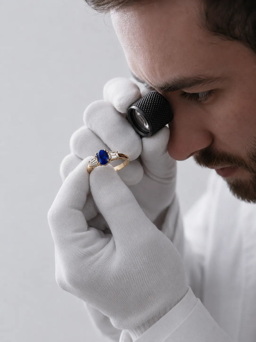 Finished SARATTI oval blue sapphire and diamond gold ring examined under a jeweler’s loupe for final quality inspection
