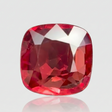 Square-cut red gemstone on a reflective surface with a light gray background