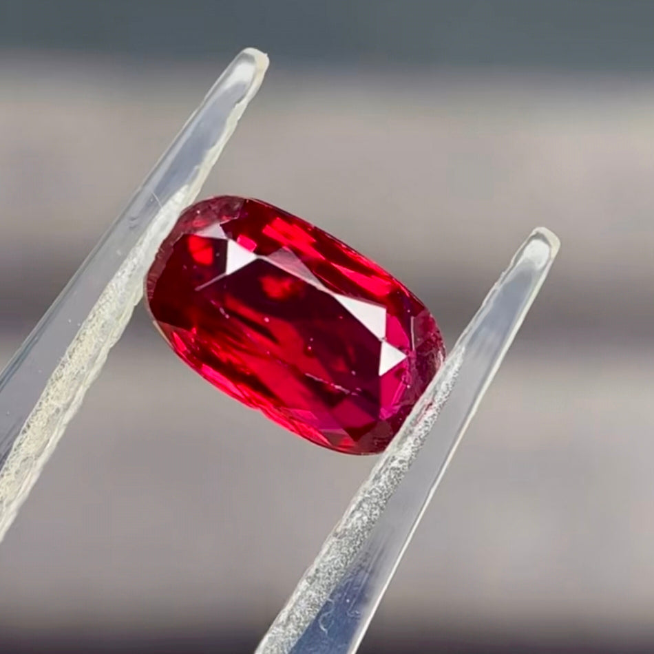 Red gemstone held between tweezers against a blurred background |  Unheated Mozambique ruby 0.89ct oval shape loose stone | SARATTI