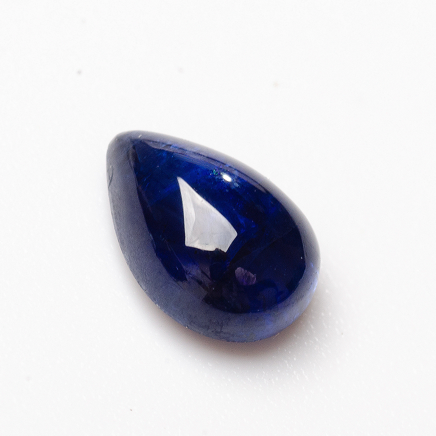Pear cabochon blue sapphire gemstone close-up on natural surface | SARATTI