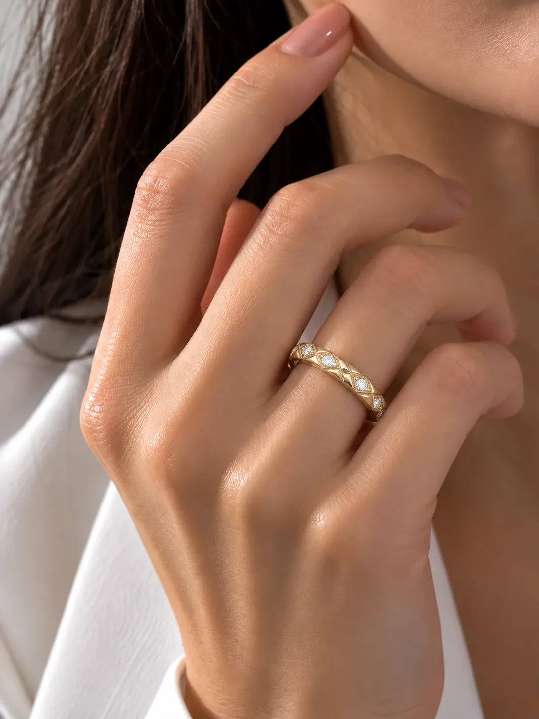 A close-up of a woman's hand wearing a delicate gold band ring adorned with small white pearls, set against a soft white garment background.