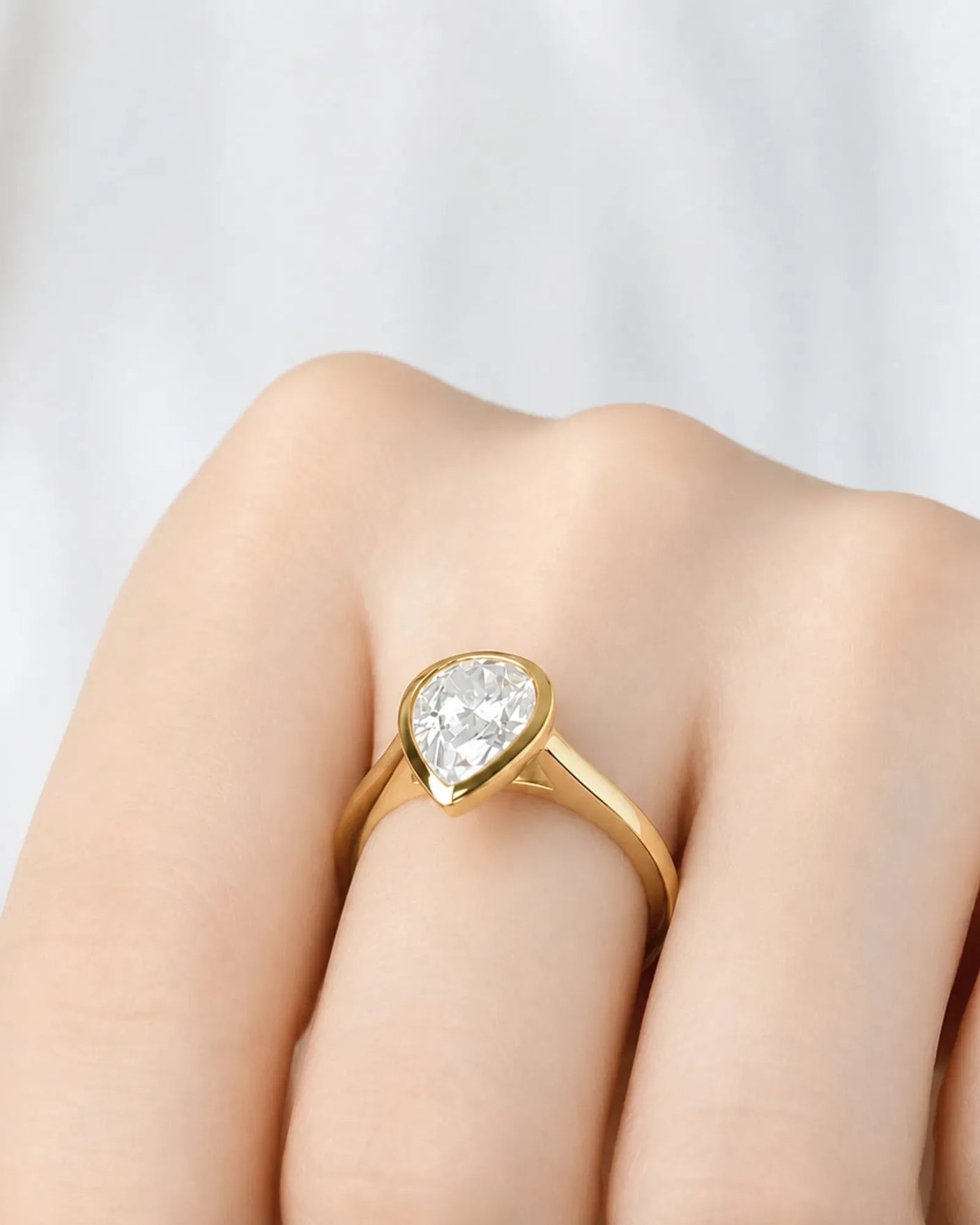 Aurelia's Embrace 1 carat pear-cut natural diamond bezel engagement ring in 18K yellow gold, worn on hand | SARATTI