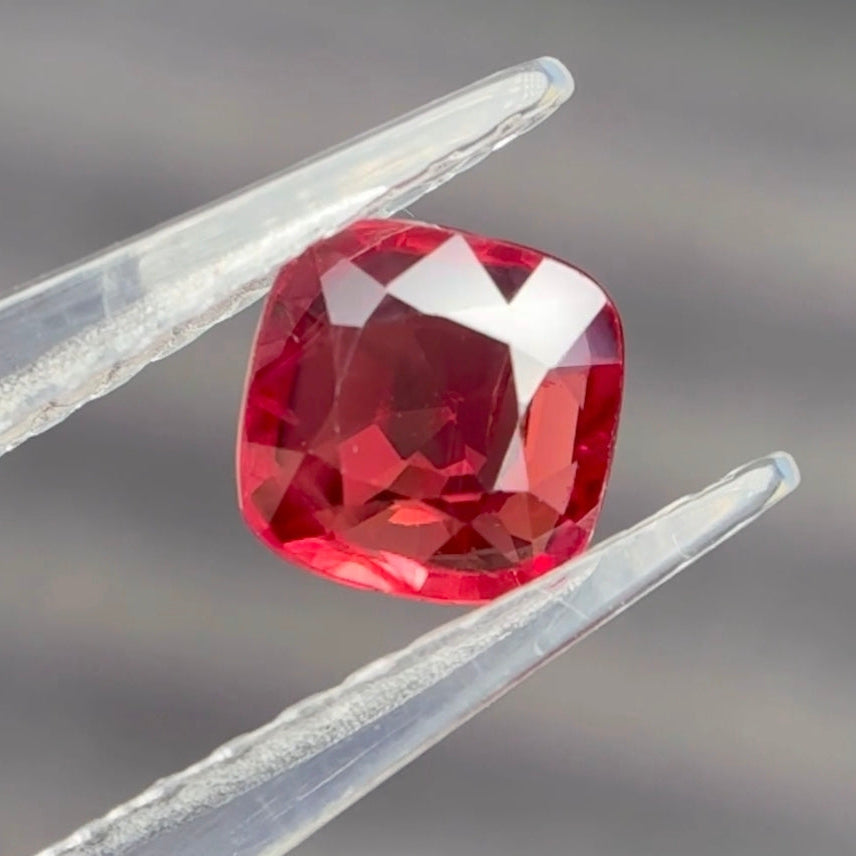 Red gemstone held between tweezers against a blurred background