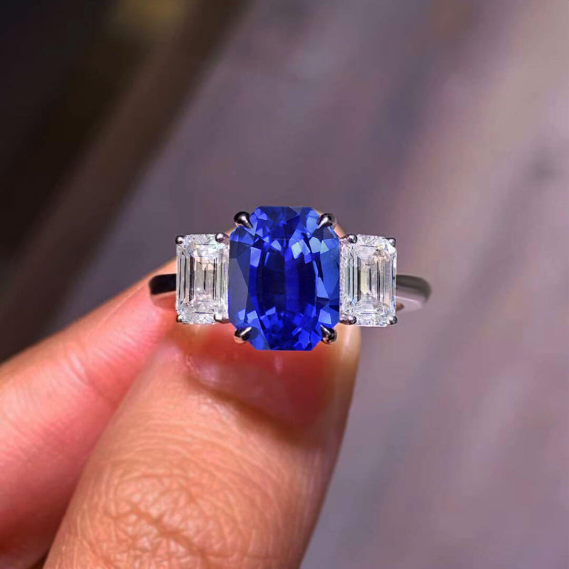 Beautiful Three Stone Emerald Cut Sapphire Ring Held up between fingers - Sapphire Engagement Ring Settings and Styles for 2023 – Saratti